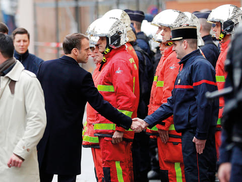 French President Emmanuel Macron (L) shakes hands with a firefighter during a visit in the streets of Paris on December 2, 2018, a day after clashes during a protest of Yellow vests (Gilets jaunes) against rising oil prices and living costs. 