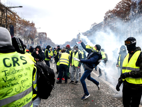 Protestors wearing "yellow vests" send back tear gas canisters during clashes with riot police (unseen) during a protest against rising costs of living in the Champs Elysees in Paris