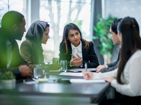 A multi-ethnic group of business people are indoors in an office boardroom.