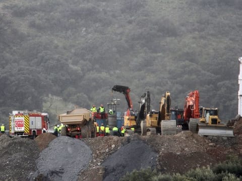 Drill and excavating machinery work on top of the mountain next to a deep borehole to reach a trapped 2-year-old boy.