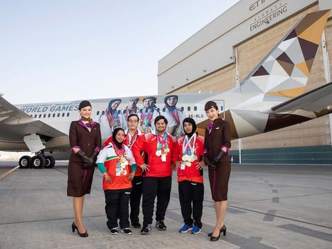 Special Olympics athletes infront of the branded Boeing 787-9 flanked by Etihad Airways Cabin Crew