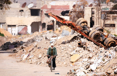 A man rides on a bike past rubble in Ein Terma, a district of eastern Ghouta, Syria 