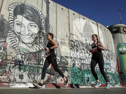 Athletes run past a mural depicting the Palestinian Leila Khaled, the 1970 Popular Front for the Liberation of Palestine (PFLP) El Al aircraft hijacker, drawn along Israel's controversial separation barrier in the biblical town of Bethlehem in the occupied West Bank during the 7th International Palestine Marathon on March 22, 2019.