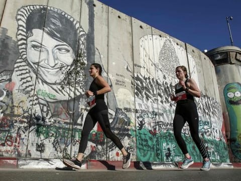Athletes run past a mural depicting the Palestinian Leila Khaled, the 1970 Popular Front for the Liberation of Palestine (PFLP) El Al aircraft hijacker, drawn along Israel's controversial separation barrier in the biblical town of Bethlehem in the occupied West Bank during the 7th International Palestine Marathon on March 22, 2019.