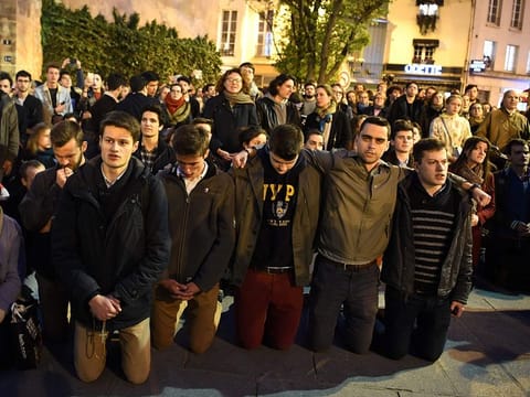 People kneel on the pavement as they pray outside watching flames engulf Notre-Dame Cathedral in Paris on April 15, 2019. 