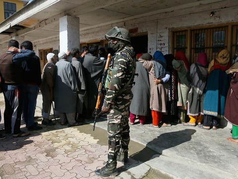 An Indian paramilitary soldier stands guard as Kashmiri voters wait in a queue to cast their votes outside a poling station during the second phase of India's general elections, on the outskirts of Srinagar, Indian controlled Kashmir.