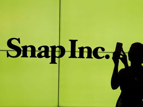 A woman stands in front of the logo of Snap Inc. 