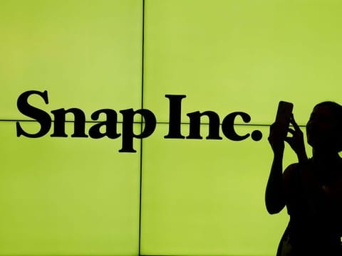 A woman stands in front of the logo of Snap Inc. 