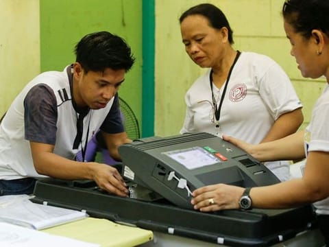 Election workers try to fix a jammed ballot inside a counting machine at a polling center in the Manuel L. Quezon elementary school, Manila, Philippines.
