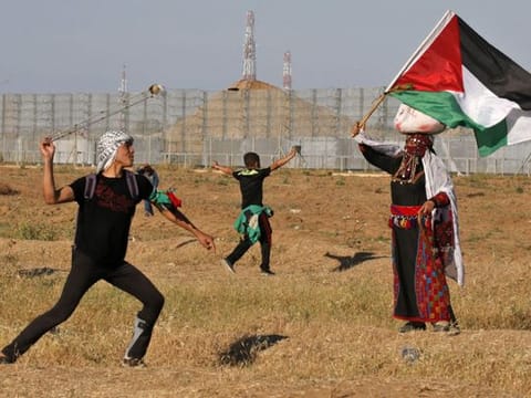 A protester hurls stones at Israeli troops as a woman wearing a traditional Palestinian outfit waves a national flag, during a demonstration near the border with Israel, east of Gaza City, on May 10, 2019.