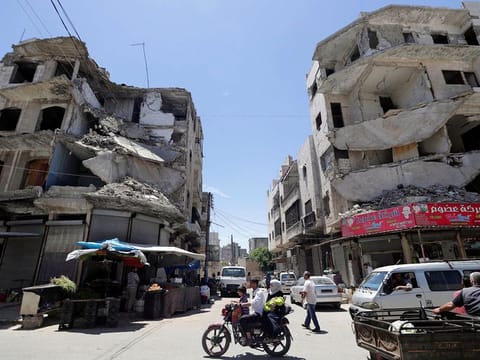 A man rides on a motorbike with his family past damaged buildings in the city of Idlib, Syria.