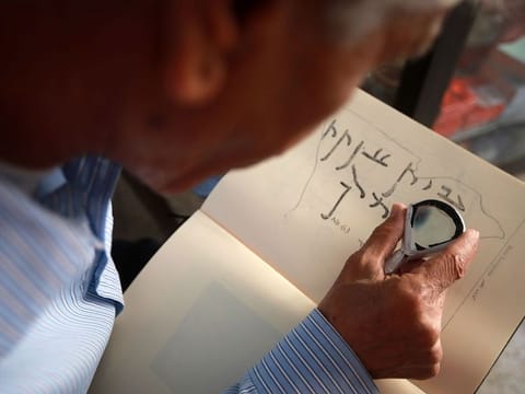 George Zaarour, a specialist in the Aramaic language, uses a magnifying glass to decipher Aramaic script in the Syrian mountain village of Maalula, in the Damascus 