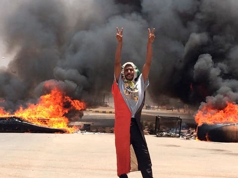 A protester flashes the victory sign in front of burning tires and debris on road 60, near Khartoum's army headquarters, in Khartoum, Sudan, Monday, June 3, 2019. 