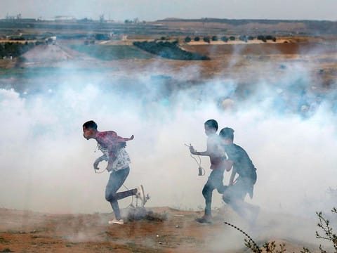 Palestinian protesters walk away through fumes from tear gas fired by Israeli forces across the barbed wire fence during a protest marking Al Quds (Jerusalem) International Day along the border near Bureij in the central Gaza Strip on May 31, 2019.