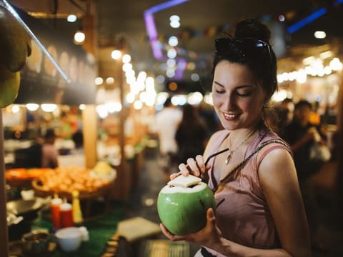 Authentic Thai street food in Bangkok. Young woman is having a refreshment with delicious coconut water on a hot summertime evening.