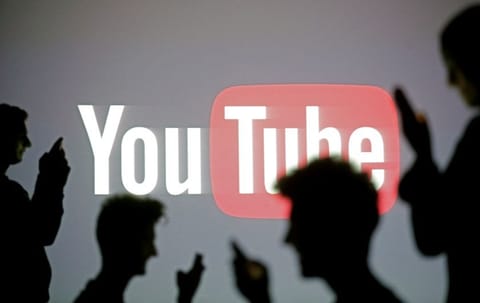 People pose with mobile devices in front of a screen projected with a YouTube logo
