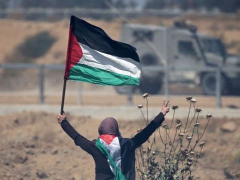 A woman holding a Palestinian flag gestures in front of Israeli forces during a protest marking the 71st anniversary of the 'Nakba', or catastrophe, when hundreds of thousands fled or were forced from their homes in the war surrounding Israel's independence in 1948, at the Israel-Gaza border fence, in the southern Gaza Strip on May 15, 2019. 