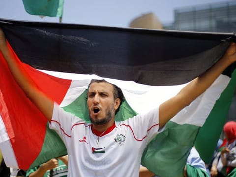 A Palestinian holds up a Palestine flag as he chants slogans during a demonstration against a US-sponsored Middle East economic workshop in Bahrain, in front of the United Nations headquarters in Beirut, Lebanon, on June 25, 2019. 