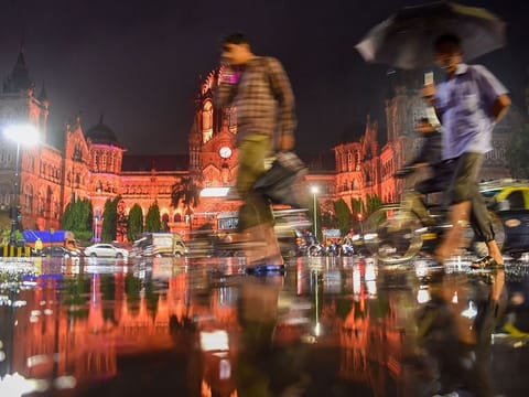 People pass in front of Chhatrapati Shivaji Terminus as it rains  in Mumbai.