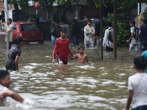Indian children walk along a flooded street after heavy rain showers in Mumbai.