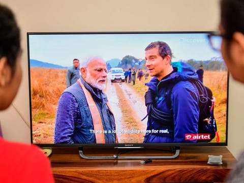 People watch on television the special edition of 'Man Vs Wild' series hosted by survival expert Bear Grylls (R), going on a mission with Indian Prime Minister Narendra Modi, in Bangalore on August 12, 2019.