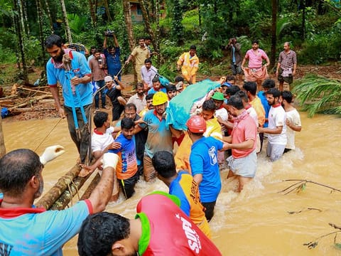 Rescue workers help locals who carry a dead body to cross a waterlogged area, after a landslide, at Kavalappara in Malappuram, on August 11, 2019.  