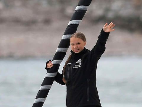 Swedish climate activist Greta Thunberg waves from aboard the Malizia II IMOCA class sailing yacht off the coast of Plymouth, southwest England, on August 14, 2019, as she starts her journey across the Atlantic to New York where she will attend the UN Climate Action Summit next month.