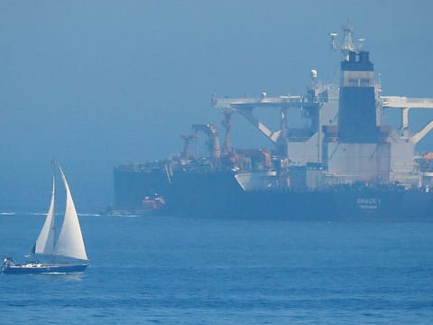 A sailboat sails as a boat approaches to the boarding ladder of the Iranian oil tanker Grace 1 as it stays anchored after it was seized last month by British Royal Marines in the Strait of Gibraltar.