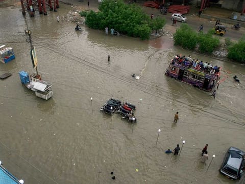 An overloaded bus drives through a flooded road caused by heavy monsoon rains, in Karach