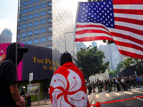 A protester wraps himself with Hong Kong flag, with the U.S. flag seen at right, as they march from Chater Garden to the U.S. Consulate in Hong Kong