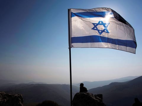 An Israeli occupation soldier stands guard under an Israeli national flag during a tour made by Israeli parliament members in the Jordan Valley near the Jewish colony of Maale Efrayim January 2, 2014.