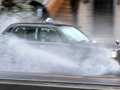 A taxi carrying passengers speeds through water covering a road in the Aoyama district of Tokyo on October 12, 2019, as the effects of Typhoon Hagibis started to be felt in Japan's capital.