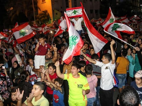 Youths wave Lebanese national flags as they gather during a demonstration on the eighth day of protest against tax increases and official corruption in the southern city of Sidon on October 24, 2019.  / AFP / Mahmoud ZAYYAT