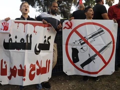 Palestinian citizens of Israel carry a placard reading in Arabic, "enough with violence, arms are destroying us" as they protest outside the district police headquarters in the Arab Israeli city of Nazareth during a demonstration against violence, organised crime and recent killings among their communities, on October 22, 2019.  