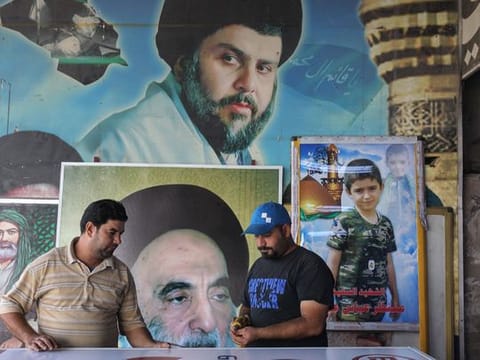 Iraqi men work in front of posters bearing the portraits of Iraqi Shiite cleric and political leader Moqtada al-Sadr 