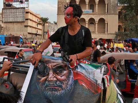 In this Nov. 3, 2019, file photo, protester hits a poster showing the leader of the Iranian Revolutionary Guard's foreign wing, or Quds Force, Gen. Qassim Soleimani with a shoe during ongoing anti-government protests in Baghdad, Iraq.