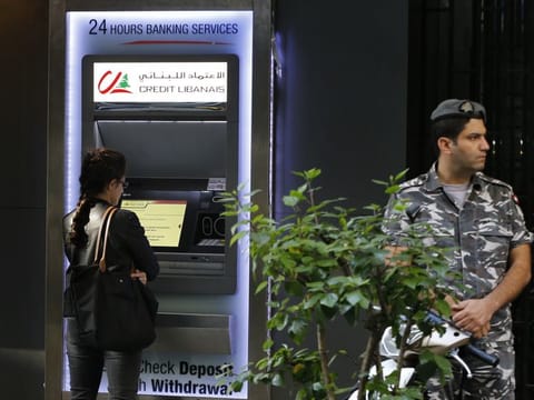 A woman uses ATM outside a bank, as a Lebanese policeman stands guard, in Beirut, Lebanon, Wednesday.