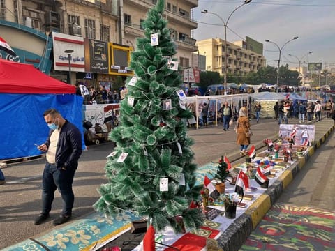 People pass by a Christmas tree with portraits of anti-government protesters who killed under fire from security forces in Tahrir Square during ongoing protests in Baghdad, Iraq, Thursday, Dec. 12, 2019. A gunman shot dead several people, including four protesters, Thursday provoking some anti-government demonstrators to disarm and hang him in a central Baghdad square, security and health officials said. The incident was condemned by the wider protest movement based in Tahrir Square, the epicenter of the movement, who said the individuals who killed the gunman were not part of their peaceful demonstrations. 