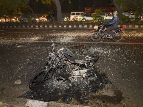 New Delhi: A motorcyclist rides past a charred vehicle after a protest against Citizenship Act at Mathura Road, in New Delhi, Sunday, Dec. 15, 2019