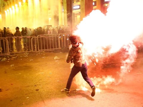 An anti-government protester throws flares against the riot police, background, during a protest near the parliament square, in downtown Beirut, Lebanon, Sunday, Dec. 15, 2019. 