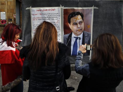 Protesters take pictures with their mobile phones of a defaced poster of newly-nominated Lebanese Prime Minister, Hassan Diab, and a list of what the protesters call the premier's achievements when he was minister of higher education, in downtown Beirut, Lebanon, Sunday, Dec. 22, 2019. 