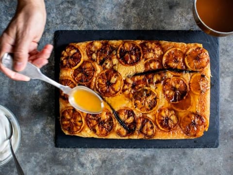 Lemon-maple butter is drizzled onto Yotam Ottolenghi’s upside-down lemon sponge cake, still warm from the oven, in New York, Dec. 8, 2019. Wrapping a cake with parchment paper and foil before it gets its long, slow bake ensures not only the “ta-da!” element once it’s revealed, but also the retention of flavor and moisture within the cake when it’s served. (Andrew Scrivani/The New York Times)