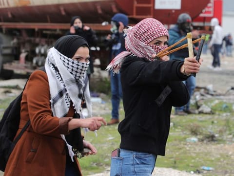 A Palestinian demonstrator uses a sling shot to hurl rocks at Israeli occupation forces during clashes following rally protesting a US peace plan proposal, at the northern entrance of the West Bank city of Ramallah near the Jewish colony of Beit El, on February 1, 2020. 