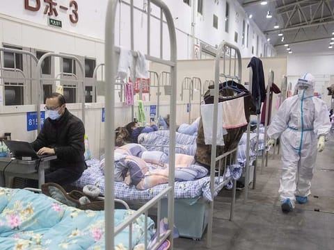 This photo taken on February 17, 2020 shows a man (L) who has displayed mild symptoms of the COVID-19 coronavirus using a laptop at an exhibition centre converted into a hospital in Wuhan in China's central Hubei province. 
