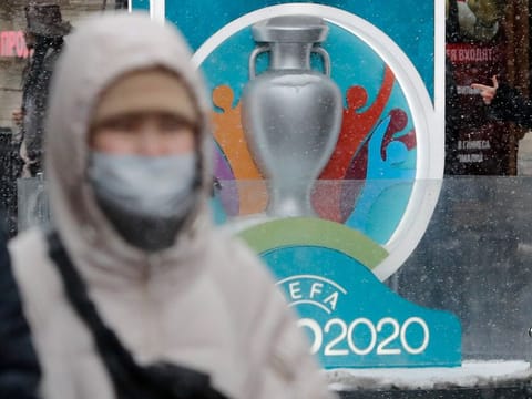 A person wearing a protective face mask walks past the Euro 2020 countdown clock in central Saint Petersburg, Russia. 