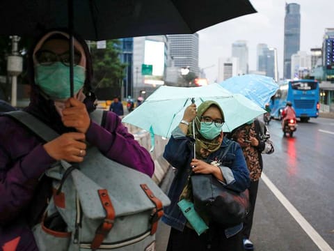 Women wearing protective masks stand at the sidewalk as they wait for a bus during rush hour, after Indonesia confirmed its first cases of COVID-19, in Jakarta, Indonesia.