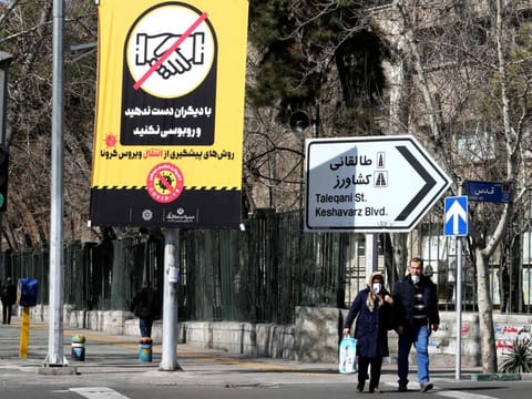 Iranians wearing protective masks walk under a prevention campaign poster for coronavirus  on March 4 in Tehran. 