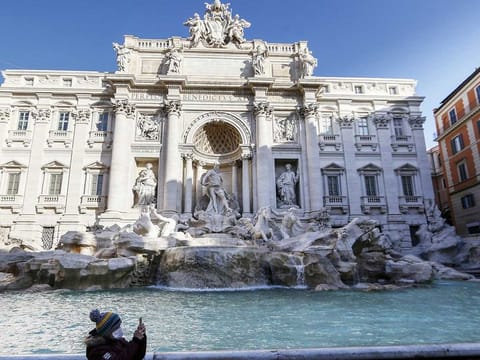 A girl wearing a mask takes photos in front of the Trevi fountain, in Rome.
