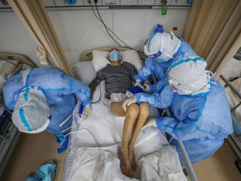 This photo taken on March 6 shows medical staff helping a coronavirus patient at the Red Cross hospital in Wuhan in China's central Hubei province. China on March 7 reported 28 new deaths from the coronavirus outbreak, bringing the nationwide toll to 3,070. 