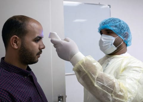 An expatriate (left) takes a coronavirus temperature test, after returning from vacation, following the outbreak of the virus, at a health clinic in Subhan, Kuwait March 9.